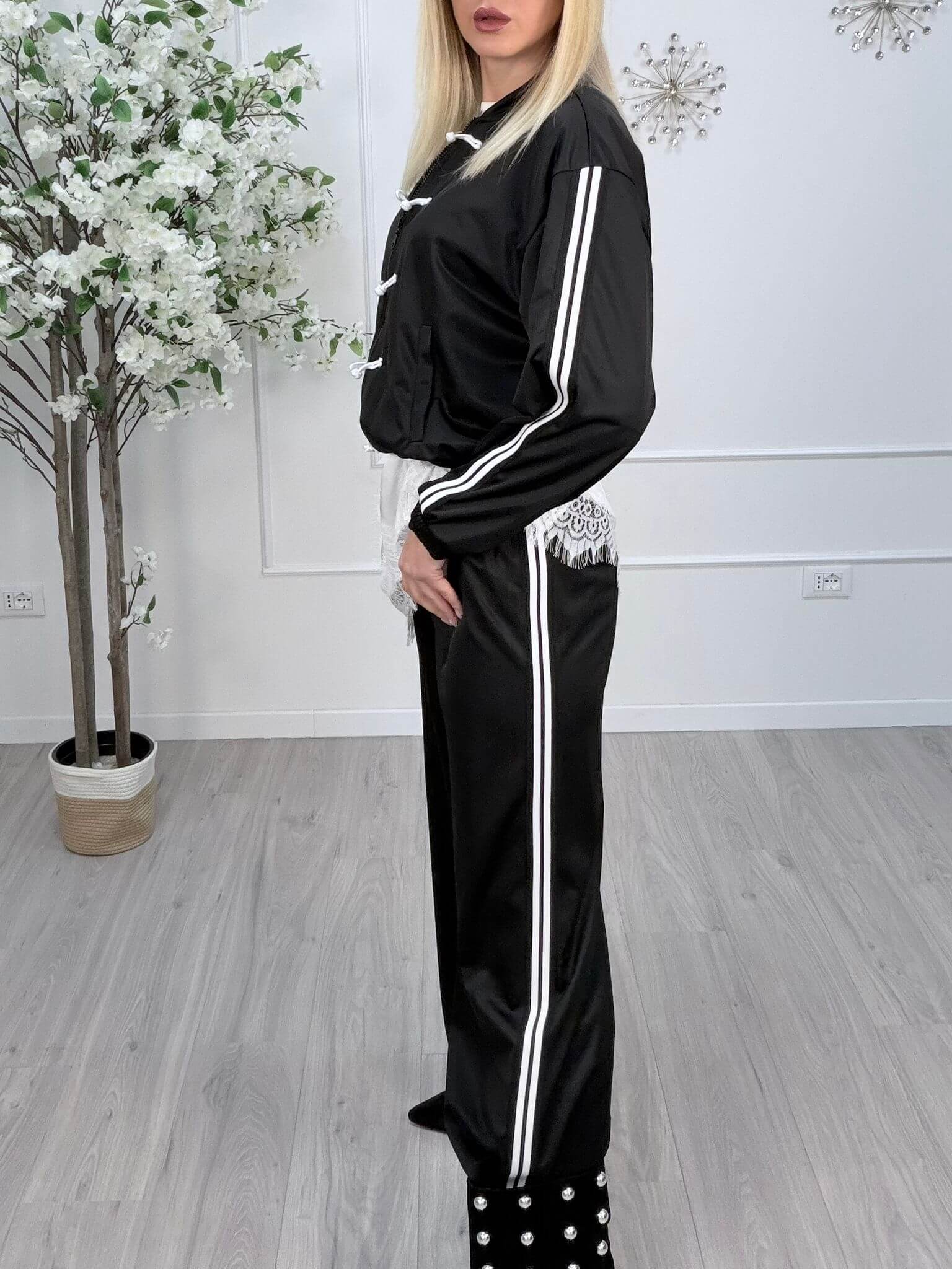 Pantaloni palazzo elastico da tuta neri con bande bianche, indossati da una modella in un ambiente moderno.