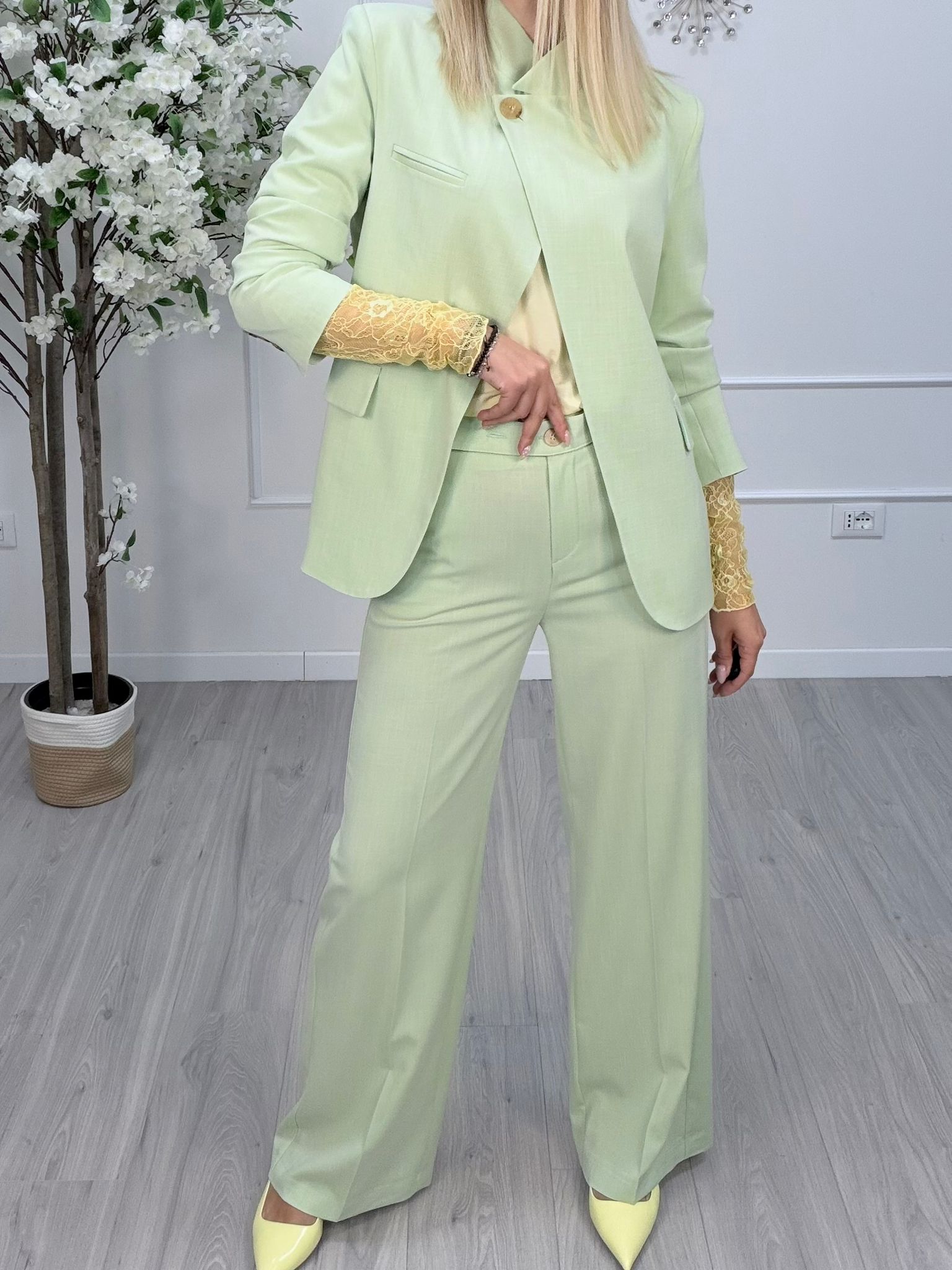 Giacca Maryley Verde Menta indossata da modella con pantaloni abbinati e top giallo, in un ambiente moderno.