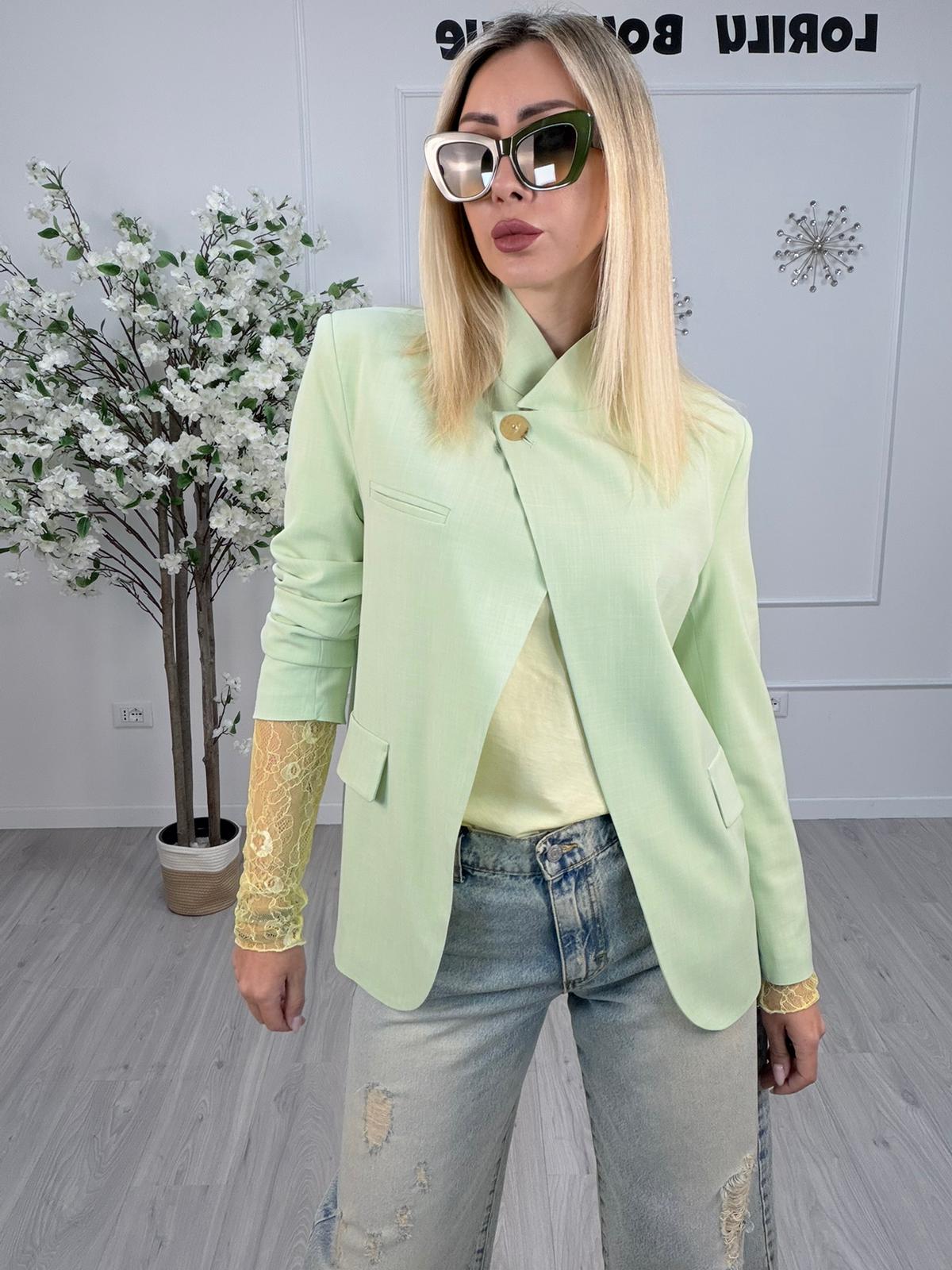Giacca Maryley Verde Menta indossata da una donna, abbinata a occhiali da sole e jeans, in un ambiente moderno.